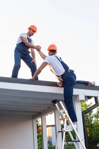 Builder helping to colleague on ladder near roof of building — Stock Photo