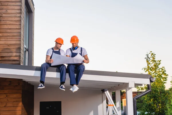 Obreros en uniforme y sombreros de trabajo con plano en el techo del edificio - foto de stock