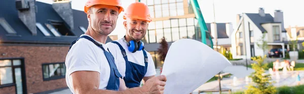 Horizontal crop of builders in hardhats holding blueprint on urban street — Stock Photo