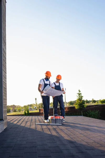 Constructeurs avec plan directeur debout près de la boîte à outils sur le toit du bâtiment — Photo de stock