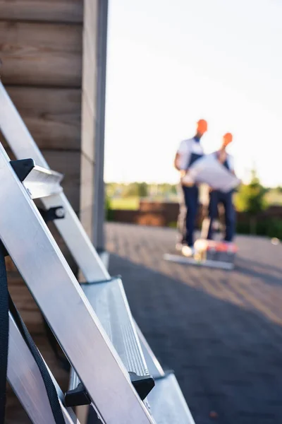 Selective focus of ladder and builders working on roof of house at background — Stock Photo