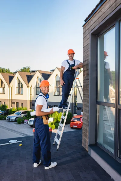 Constructeurs avec plan et échelle regardant la caméra sur le toit du bâtiment — Photo de stock