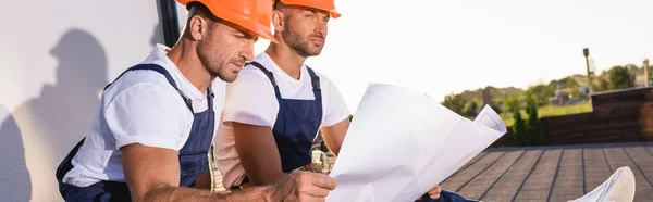 Panoramic shot of builder holding blueprint near colleague on roof of building — Stock Photo