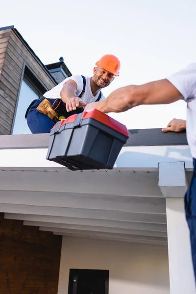 Focus selettivo del costruttore dando cassetta degli attrezzi al collega sul tetto della casa — Foto stock