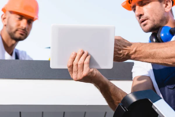 Selective focus of builders in hardhats using digital tablet while working on roof of house — Stock Photo