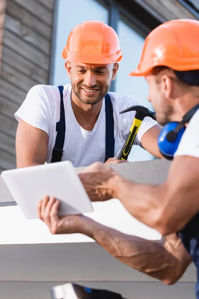 Foco seletivo do construtor segurando martelo perto colega com tablet digital no telhado do edifício — Fotografia de Stock