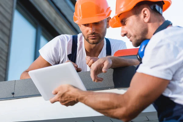 Foco seletivo de trabalhadores manuais olhando para tablet digital no telhado da casa — Fotografia de Stock