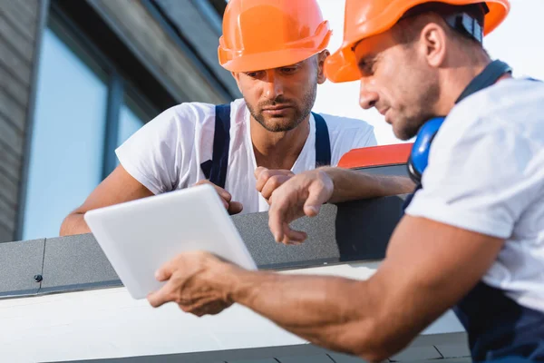 Focus selettivo degli operai che guardano tablet digitale sul tetto della casa — Foto stock