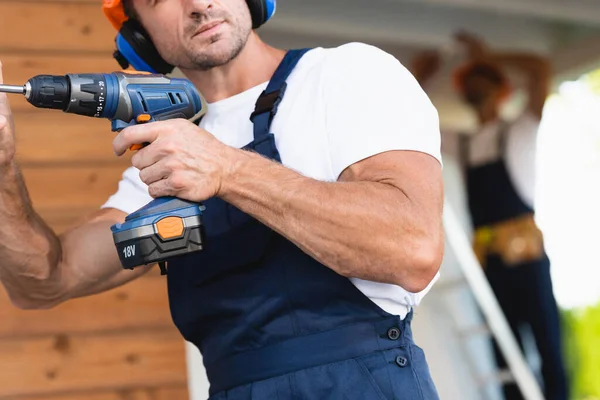 Selective focus of builder holding electric screwdriver near building — Stock Photo