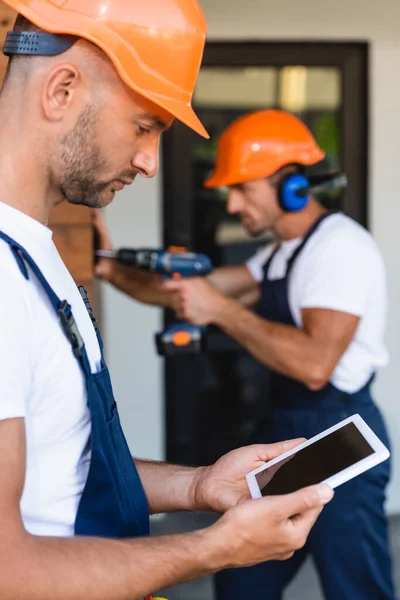 Selective focus of builder holding digital tablet near colleague working near building — Stock Photo