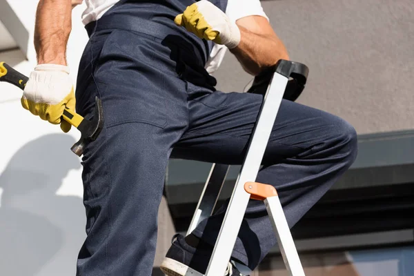 Ausgeschnittene Ansicht eines Bauarbeiters, der Hammer hält, während er auf Leiter im Freien steht — Stockfoto