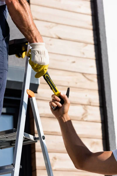 Ausgeschnittene Ansicht von Bauarbeitern mit Hammer in der Nähe von Leiter und Gebäude — Stockfoto