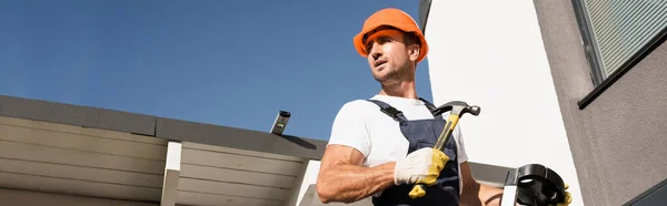 Horizontale Ernte des Bauarbeiters hält Hammer, während er auf Leiter in der Nähe des Hauses steht — Stockfoto