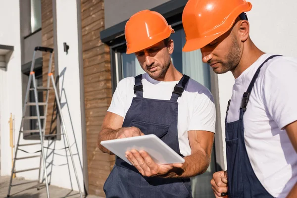 Selektive Fokussierung der Bauherren mit digitalem Tablet bei der Arbeit in der Nähe des Hauses — Stockfoto