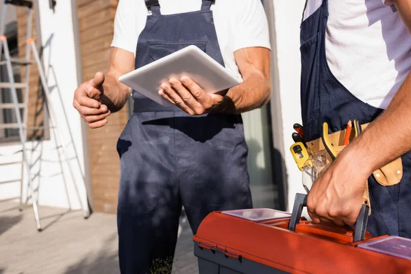 Cropped view of builder holding digital tablet near colleague with toolbox outdoors — Stock Photo