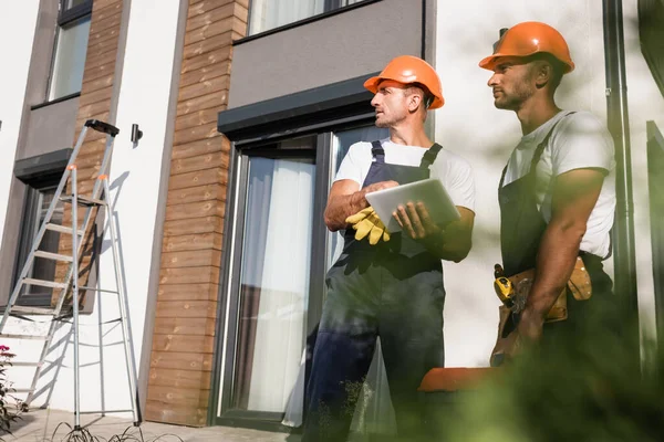 Выборочный фокус ручных рабочих с инструментарием с использованием цифрового планшета возле дома на открытом воздухе — стоковое фото