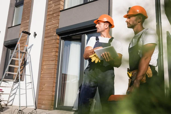 Selective focus of manual workers with toolbox using digital tablet near house outdoors — Stock Photo