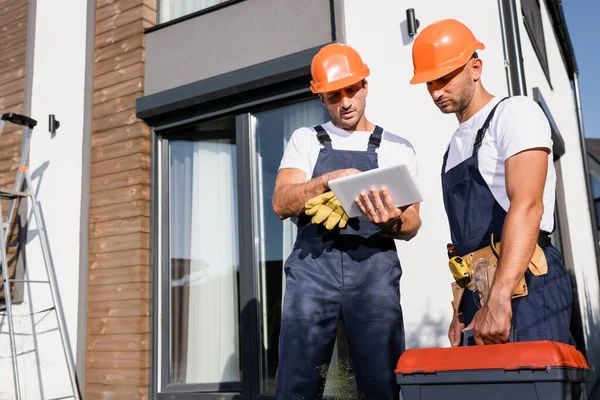 Selective focus of builders in overalls using digital tablet while working near building — Stock Photo