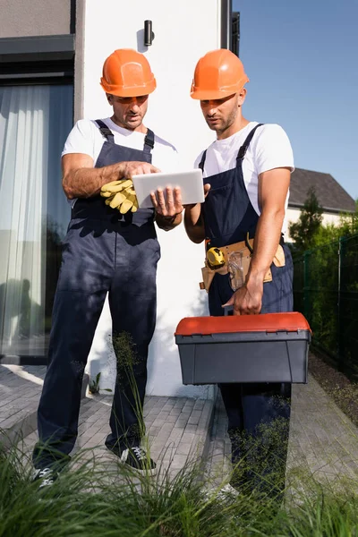 Enfoque selectivo de los constructores con cinturón de herramientas y caja de herramientas utilizando tableta digital en la calle urbana - foto de stock