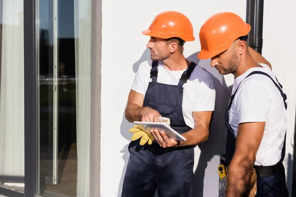 Builders in helmets using digital tablet beside building outdoors — Stock Photo