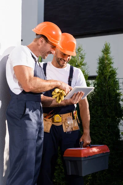 Workmen with toolbox looking at digital tablet near facade of building — Stock Photo