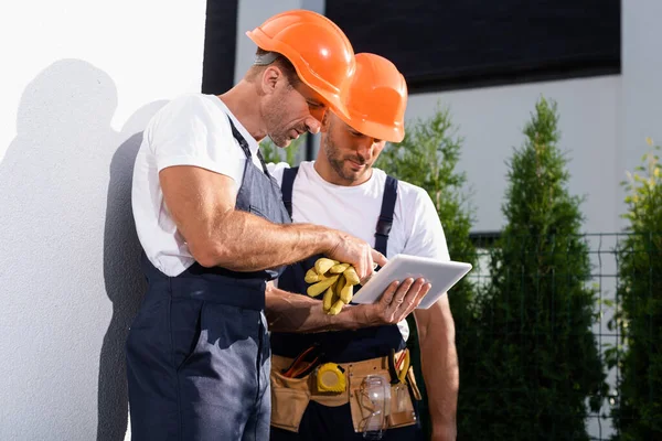 Handyman in overalls using digital tablet while standing near facade of house — Stock Photo