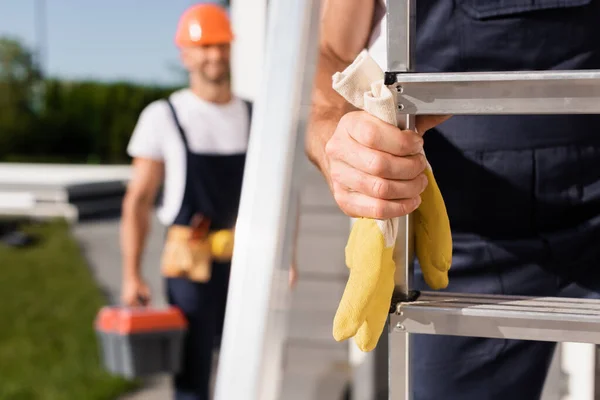 Selective focus of handyman holding gloves near ladder and colleague on urban street — Stock Photo