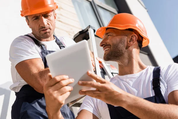 Enfoque selectivo del constructor que sostiene la tableta digital cerca de colega en la escalera cerca del edificio - foto de stock