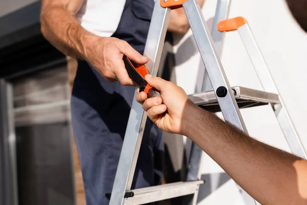 Vista ritagliata del costruttore dando pinze al collega sulla scala all'aperto — Foto stock