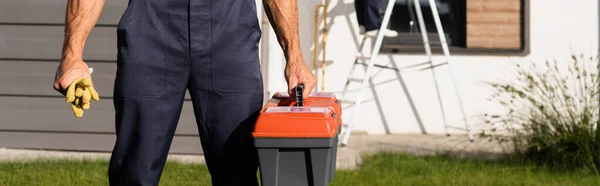 Panoramaaufnahme des Bauunternehmers mit Werkzeugkiste und Handschuhen in der Nähe von Gebäuden im Freien — Stockfoto