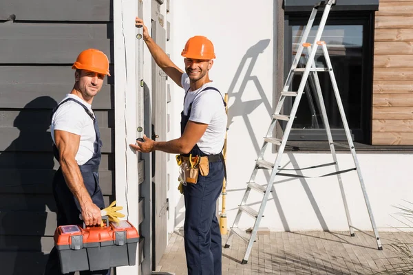 Handwerker mit Werkzeugkiste mit Wasserwaage und Blick auf Kamera in der Nähe des Hauses — Stockfoto