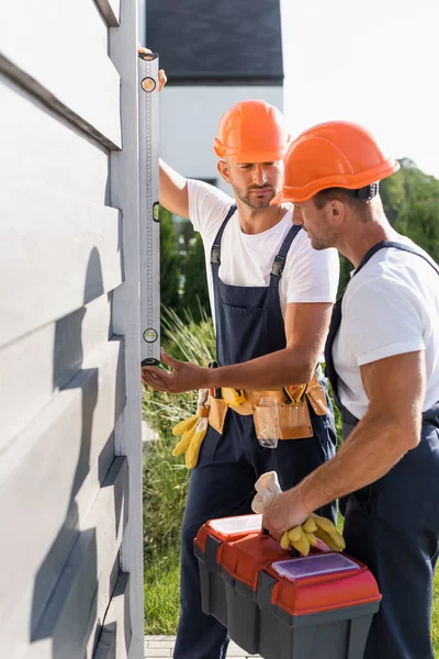 Focus selettivo degli operai con strumenti che utilizzano la livella dello spirito mentre lavorano con la facciata dell'edificio — Foto stock