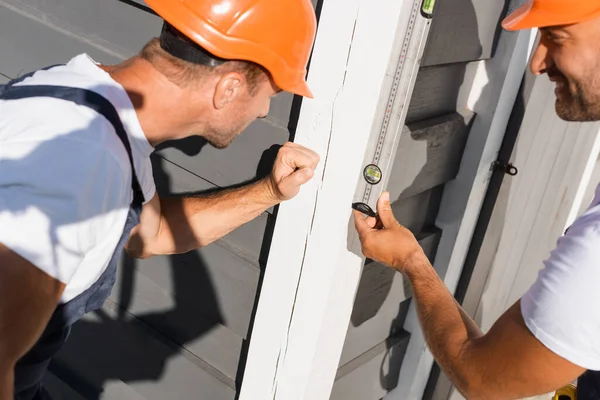 Selective focus of builders looking at spirit level while working with facade of house — Stock Photo