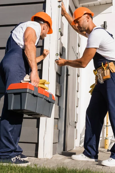 Selective focus of workmen with tools and spirit level working with facade of building — Stock Photo