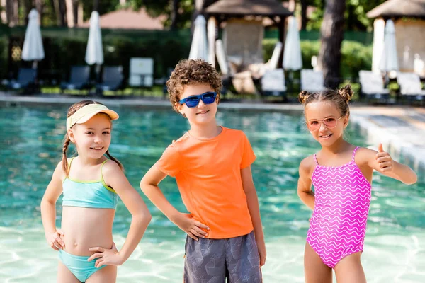 Friends standing with hands on hips while girl showing thumb up near pool — Stock Photo