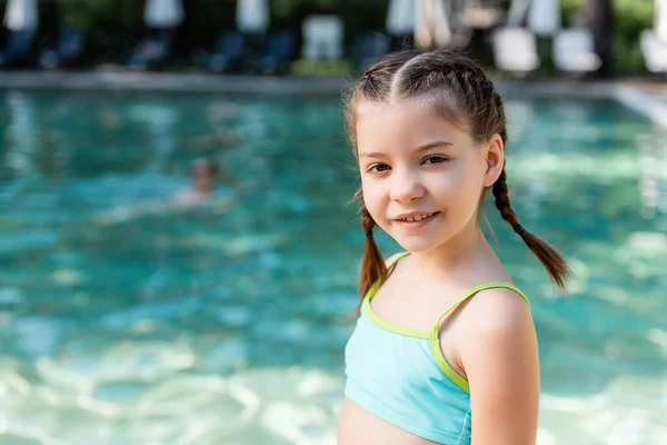 Menina em maiô olhando para a câmera enquanto posando perto da piscina — Fotografia de Stock