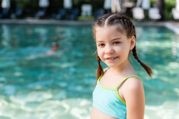 Chica en traje de baño mirando a la cámara mientras posando cerca de la piscina - foto de stock