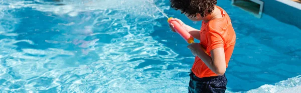 Панорамний урожай хлопчика, який грає з водяним пістолетом біля басейну — стокове фото