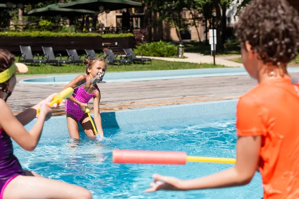 Selective focus of boy and girls fighting with water guns while having fun near pool — Stock Photo