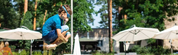 Panoramaaufnahme eines Kindes in T-Shirt und Schwimmbrille, das springt und die Nase stopft — Stockfoto