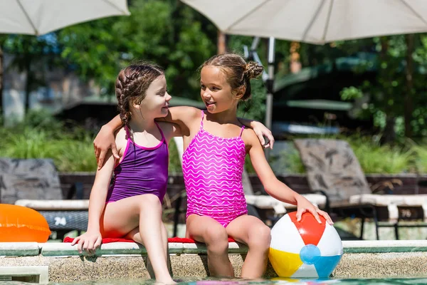 Friends in swimsuits looking at each other while hugging at poolside near inflatable ball — Stock Photo