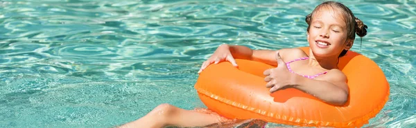Horizontales Konzept des fröhlichen Mädchens, das beim Schwimmen im Pool auf aufblasbarem Ring mit geschlossenen Augen den Daumen nach oben zeigt — Stockfoto