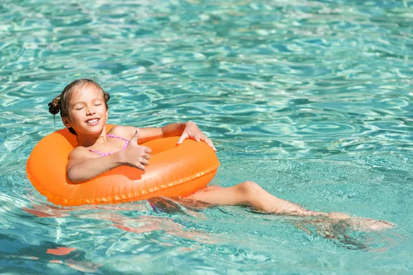 Chica complacida mostrando el pulgar hacia arriba mientras flota en la piscina en el anillo swin con los ojos cerrados - foto de stock