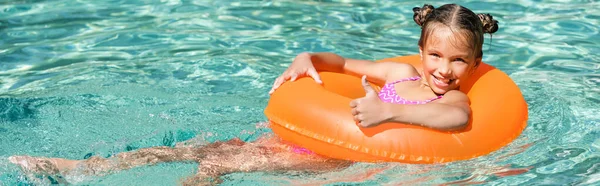 Horizontale Ernte freudiger Mädchen zeigt Daumen nach oben, während sie im Pool auf aufblasbarem Ring schwebt — Stockfoto