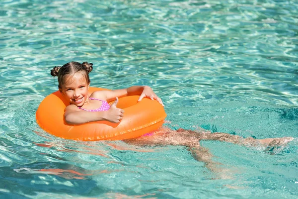Menina alegre mostrando o polegar para cima ao flutuar na piscina no anel inflável — Fotografia de Stock