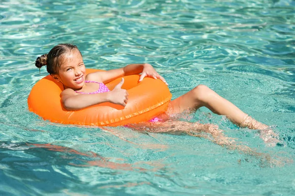 Девушка показывает большой палец вверх во время плавания в бассейне на надувном кольце — стоковое фото