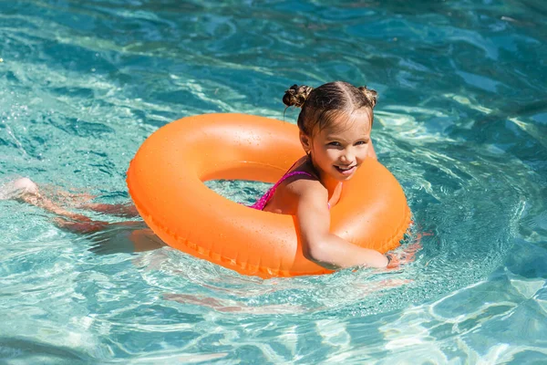 Niño mirando a la cámara mientras flota en la piscina en el anillo de natación - foto de stock