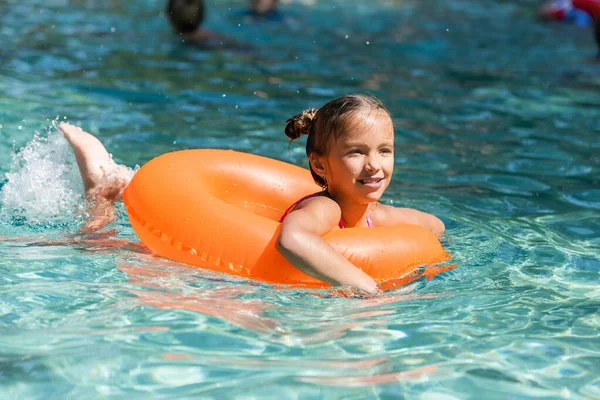 Child floating in pool on swim ring while making water splashes with legs — Stock Photo