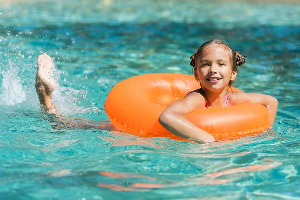 Chica flotando en la piscina en el anillo inflable y mirando la cámara - foto de stock