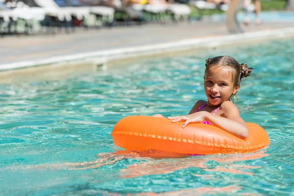 Niño flotando en la piscina en el anillo de natación y mirando a la cámara - foto de stock